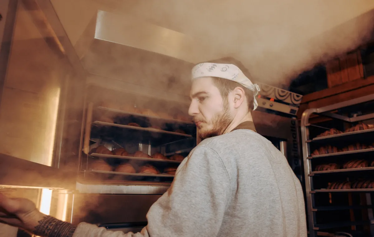 Bakery employee takes croissants out of the oven.